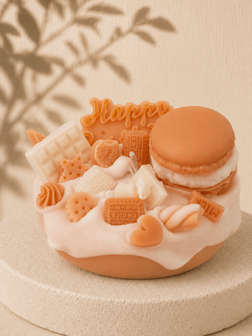 Cream Crush cake-style scented soy candle in cream and white with macaron, chocolate bars, biscuits, hearts and sweet-inspired wax decorations