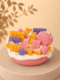 Light Pink Crush cake-style scented soy candle in light pink and white with pink, yellow and lilac wax decorations including macaron, chocolate bars, heart, biscuits and strawberries