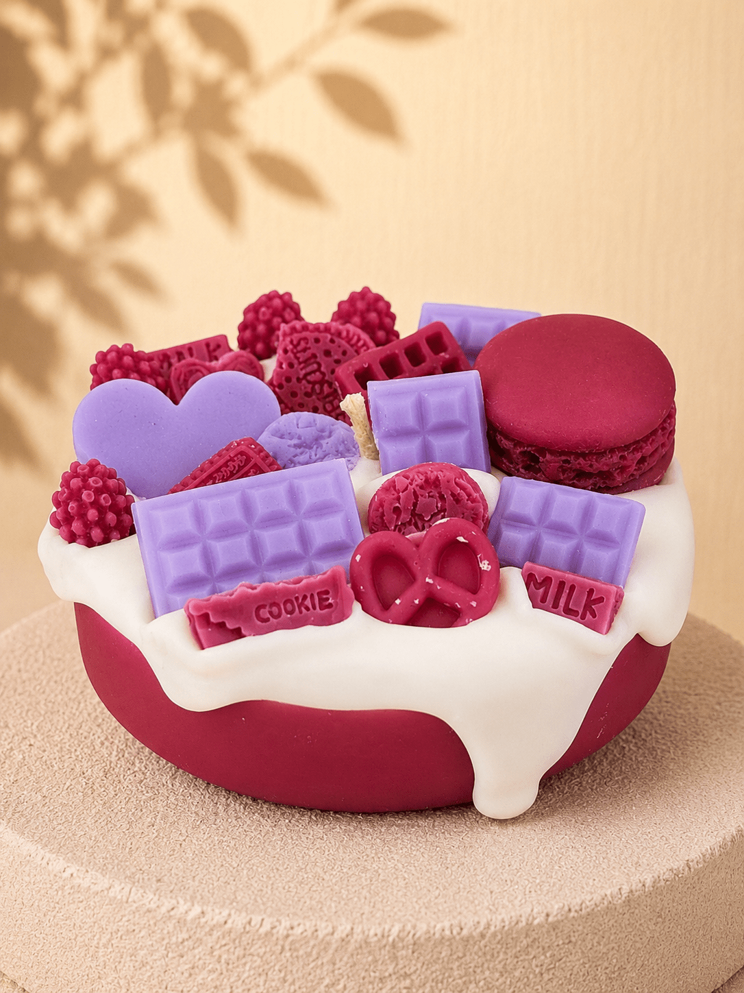 Red Velvet Crush cake-style scented soy candle in burgundy and white with burgundy and lilac wax decoration including heart, chocolate bars, berries, cookies, pretzel and macaron.