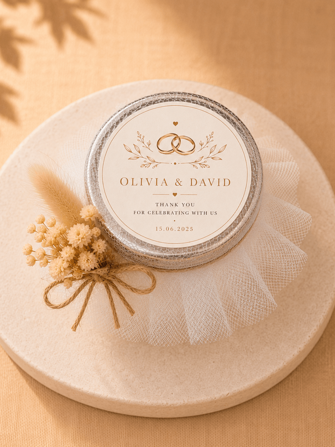 Close-up top view of a personalised wedding candle favour with bride and groom names label, tulle wrap and dried flower decoration.