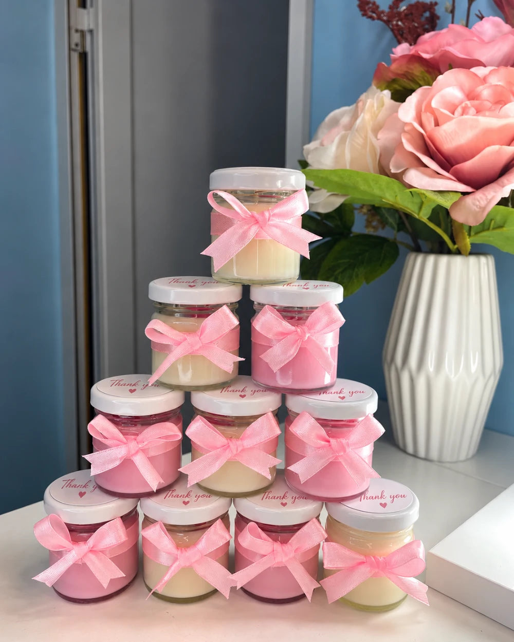 Pink and ivory personalised candle favours with matching pink ribbon bows and thank you lids