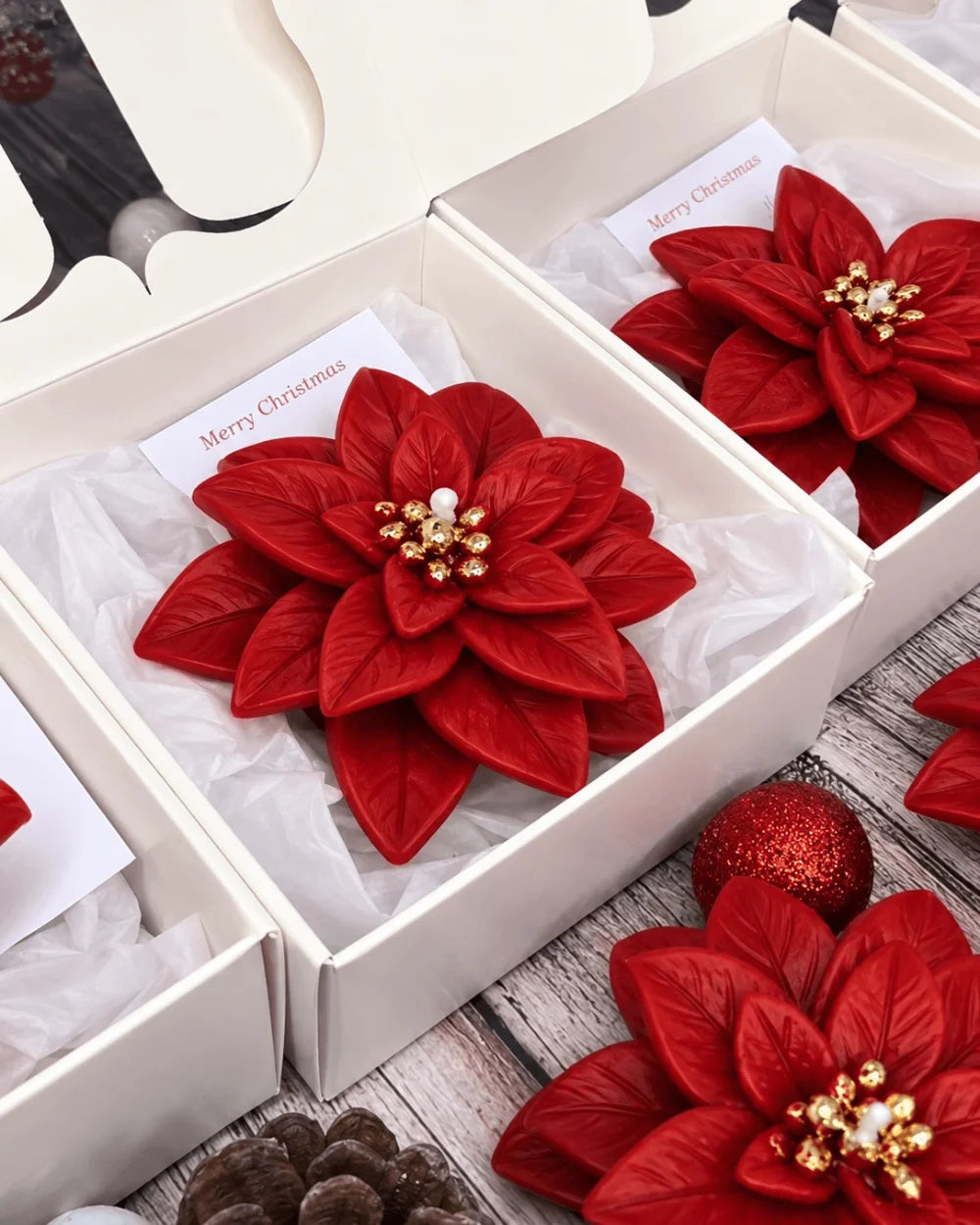 Red poinsettia Christmas candles with gold details presented in white gift boxes for corporate gifting
