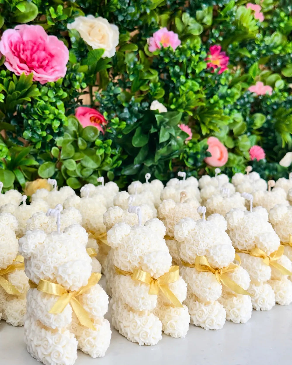 White teddy bear candle favours with yellow ribbon displayed against a floral backdrop